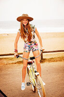A girl wearing a hat standing up on a bike