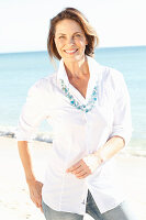 A brunette woman on a beach wearing a white shirt