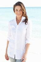 A brunette woman on a beach wearing a white shirt