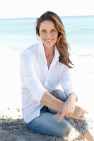 A brunette woman on a beach wearing a white shirt and jeans