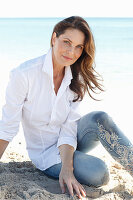 A brunette woman on a beach wearing a white shirt and jeans