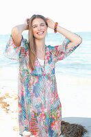 A young woman by the sea wearing a colourful beach dress