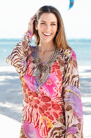 A brunette woman by the sea wearing a colourful beach dress