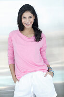 A dark-haired woman wearing a pink jumper and white shorts