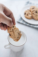 A chocolate chip being dipped into a cup of milk