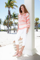 A brunette woman on the beach wearing a batik tunic and white trousers