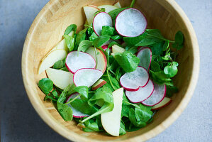 Lambs lettuce with apple and radish slices in a wooden bowl