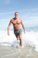 Grauhaariger Mann mit großem Tattoo in grauen Badeshorts im Meer