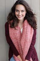 A young brunette woman wearing a wine-red cardigan with a salmon pink woollen shawl