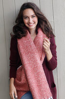 A young brunette woman wearing a wine-red cardigan with a salmon pink woollen shawl