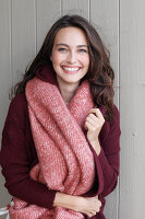 A young brunette woman wearing a wine-red cardigan with a salmon pink woollen shawl