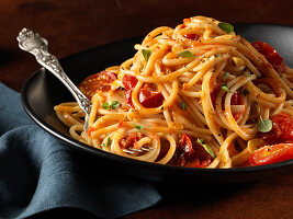 Spaghetti pasta with tomatoes and herbs in black bowl with fork