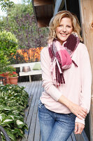 A blonde woman wearing a pink blouse, a thick scarf and jeans