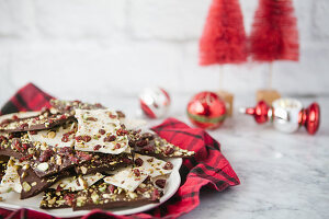 Dark and white broken chocolate with cranberries and pistachios on a plate, with baubles in the background