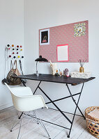 A filigree table and a white classic chair in front of a pinboard