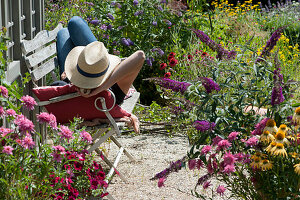 Woman relaxing on bench on gravel terrace at garden shed