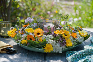 Lantern in wreath of marigold flowers, yarrow, sage, oregano flowers and vetch as table decoration