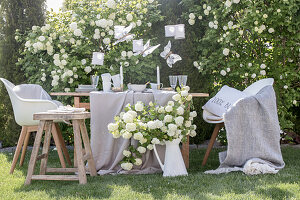 Table set in white and beige in garden in front of viburnum bush