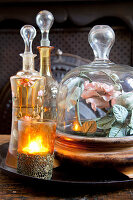 Tealight holder, antique carafes and rose under glass cover on tray