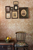 Antique chairs and trunk below framed photos on patterned wallpaper