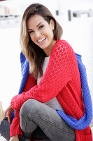 A young woman wearing a red knitted jumper with a blue jumper over her shoulders