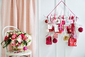 DIY advent calendar in white, red and pink with a bouquet of flowers in front of it on a chair