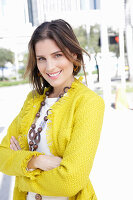 Junge Frau mit Halskette in weißem Pulli und gelber Bouclé-Jacke