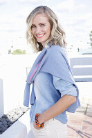 A blonde woman wearing a denim shirt with a jumper over her shoulders