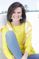 A young woman wearing a long-sleeved yellow top and jeans with a jumper over her shoulders