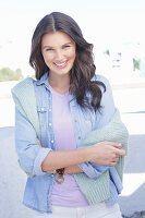 A young woman wearing a purple t-shirt and a denim shirt with a jumper over her shoulders