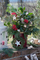 Weihnachtsstrauß mit Kiefer, Tanne, Kirschlorbeer, Skimmie und Stechpalme im Eimer auf der Gartenmauer