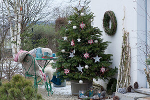 Nordmann fir decorated with stars and balls as a Christmas tree on the terrace, small seating area, chairs with fur