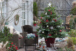 Weihnachtsterrasse mit geschmückter Nordmanntanne als Weihnachtsbaum, Korbsessel mit Fell als Sitzplatz