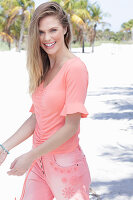 A long-haired woman wearing a short-sleeved salmon-coloured top and jeans