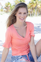 A long-haired woman wearing a short-sleeved salmon-coloured top and denim shorts