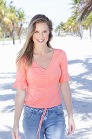 A long-haired woman wearing a short-sleeved salmon-coloured top and jeans