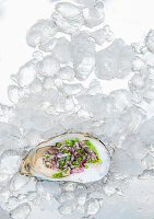 An open oyster with chives and onions on ice