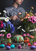 Ostertisch mit Gugelhupf, Ostereiern und Blumen, Frau im Hintergrund