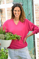 Junge Frau in pinkfarbenem Pullover hält Schale mit frischen Kräutern