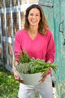 A young woman with a bowl of fresh herbs wearing a pink jumper