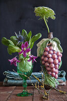 Unusual arrangement of clematis, sea holly and pak choi in wine glass and bishop's flower in ceramic vase