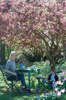 Sitzgruppe unter Zierapfelbaum 'Paul Hauber', Frau mit Kaffeetasse, Junge sitzt und liest, Hund Zula