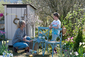 Frau mit Sohn am Gerätehaus im Garten, Zierkirsche 'Kojou no mai', Tulpen in Körben, Obststiege mit Samentüten