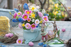 Colorful bouquet in a teapot: a daisies, primroses, grape hyacinths, daffodils and twigs, Easter bunnies and Easter eggs as decoration