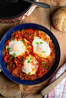 Shakshuka in a pan on an olive wood plate with bread (Tunisia)