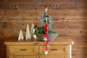 Arrangement with amaryllis and stars on red ribbons on chest of drawers