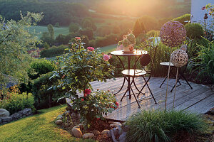 Round wooden terrace on the slope, with a patio set and roses