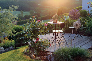 Runde Holzterrasse am Hang, mit Sitzplatz und Rosen