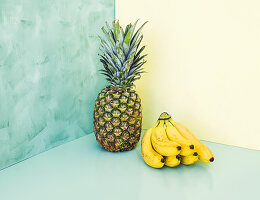 Whole ananas and bunch of bananas over yellow and green background