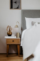 Vase and lamp on wooden bedside table next to bed with headboard